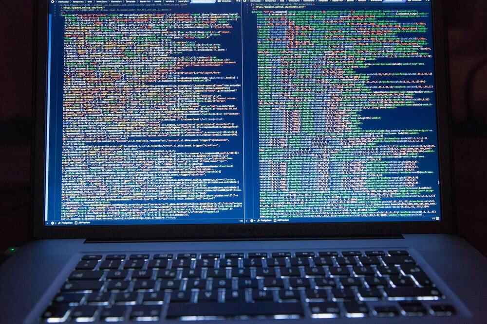 Professional developer laptop computer displaying colorful programming code on dark background for software development