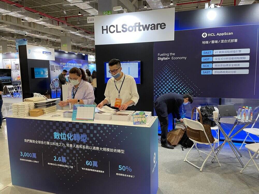 HCL AppScan trade show booth with staff, promotional signage showing DAST, IAST, SCA, SAST capabilities and digital metrics display